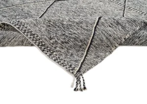 The description unveils a close-up of a black and white patterned rug corner adorned with tassels. Its intricate geometric line designs and rich texture add an elegant touch to any space, making it a pivotal decor piece.