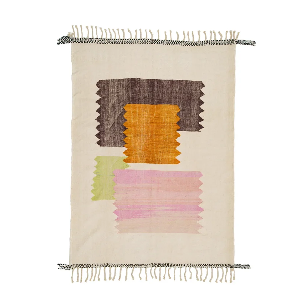 A rectangular woven rug with fringe edges, showcasing abstract designs in brown, orange, green, and pink on a beige background. This unique piece adds artistic flair to any room with its vibrant yet harmonious color palette.