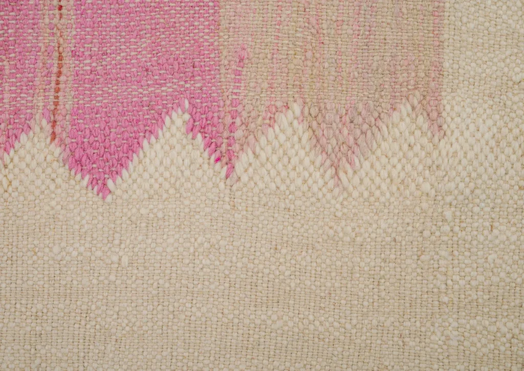 A detailed close-up of a textured fabric showcases a zigzag pattern in harmonious pink and beige hues, artfully woven into the design.