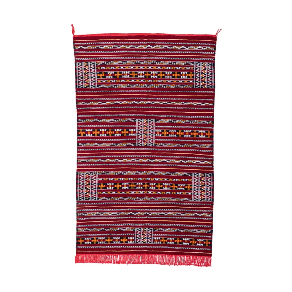 A rectangular, flatweave rug showcasing geometric patterns in red, white, black, and yellow. The design features horizontal stripes and fringed edges, adding a touch of vibrant elegance to any space.