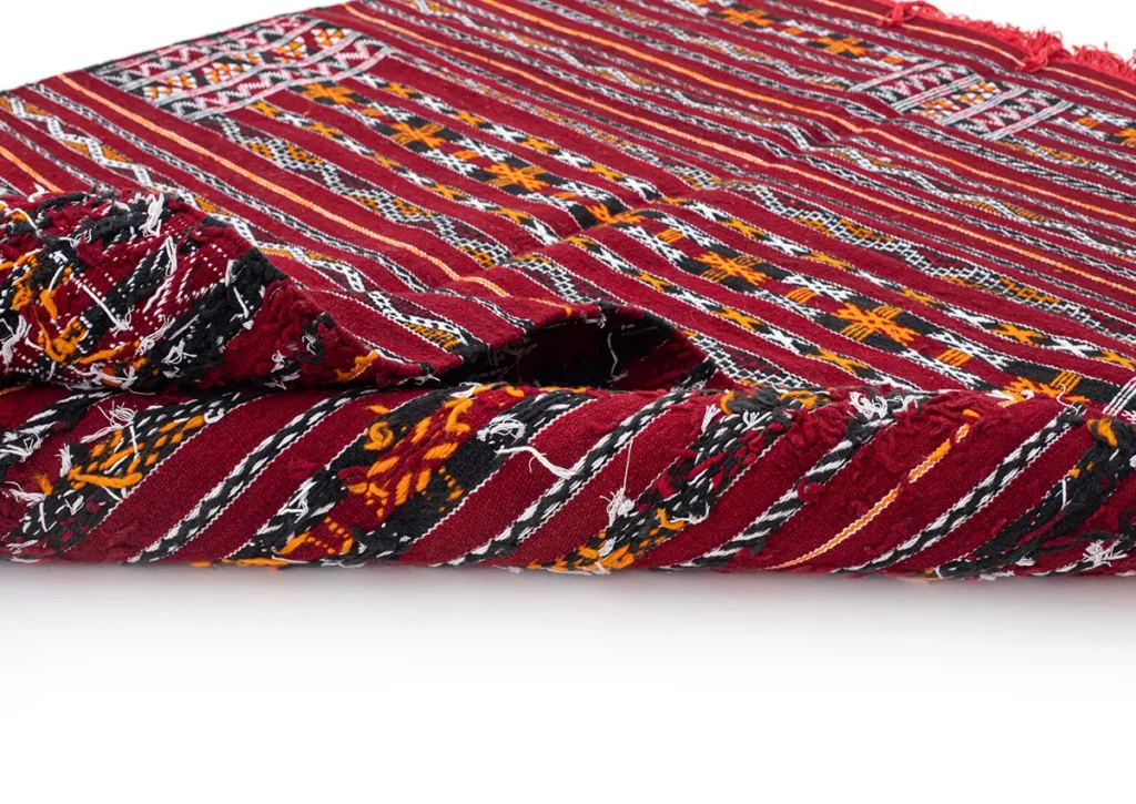 A folded section of a red flatweave rug showcases intricate patterns in yellow, black, and white stripes.