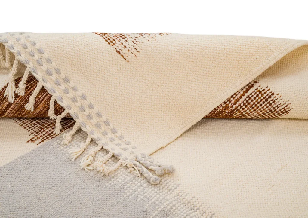 A beautifully folded beige and brown woven fabric, complete with fringe detailing on the edge, adds a touch of elegance to any décor.