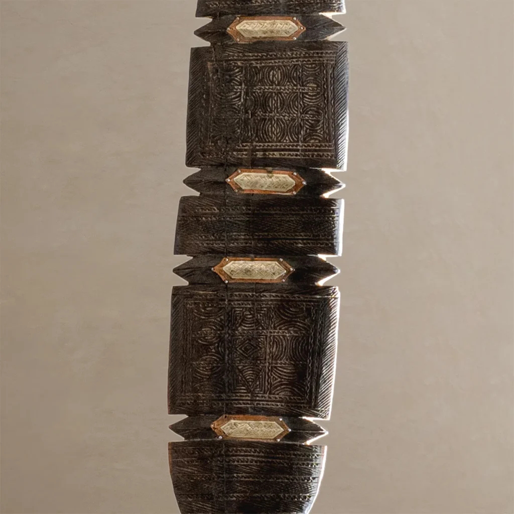Close-up of a textured, dark brown wooden structure with intricate, hand-carved details and flat, diamond-shaped inserts arranged vertically, reminiscent of vintage wooden tent pegs.
