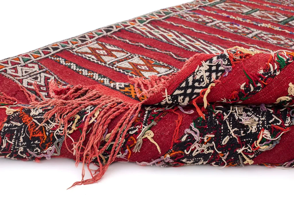 A close-up of a vintage flat rug reveals its intricate geometric patterns and multicolored fringe edges.
