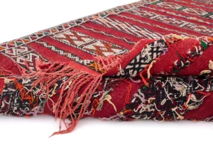 A close-up of a vintage flat rug reveals its intricate geometric patterns and multicolored fringe edges.