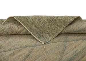 A green textured, handwoven rug is folded over at the edge, revealing its intricate reverse side.
