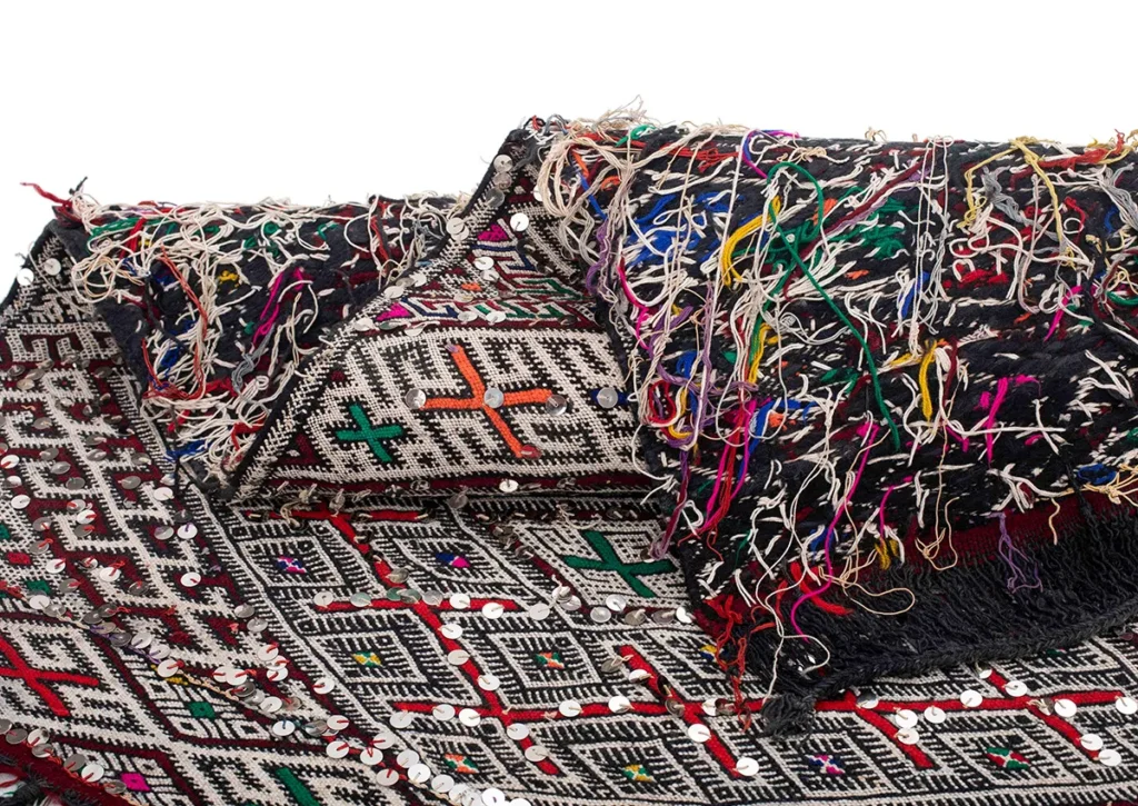 A vintage handwoven rug boasting intricate geometric patterns, colorful threads, and circular embellishments elegantly contrasts against a black background.