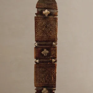 Close-up of a hand-carved wooden stick or staff adorned with intricate geometric carvings and metallic decorative elements, reminiscent of a vintage wooden tent peg.