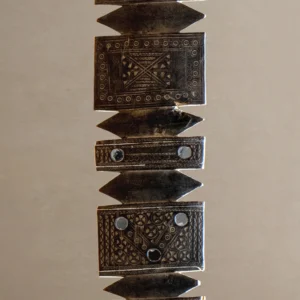 Ornate metal spearhead with geometric patterns and circular details, displayed vertically against a plain background, reminiscent of vintage wooden tent pegs in its craftsmanship and attention to detail.