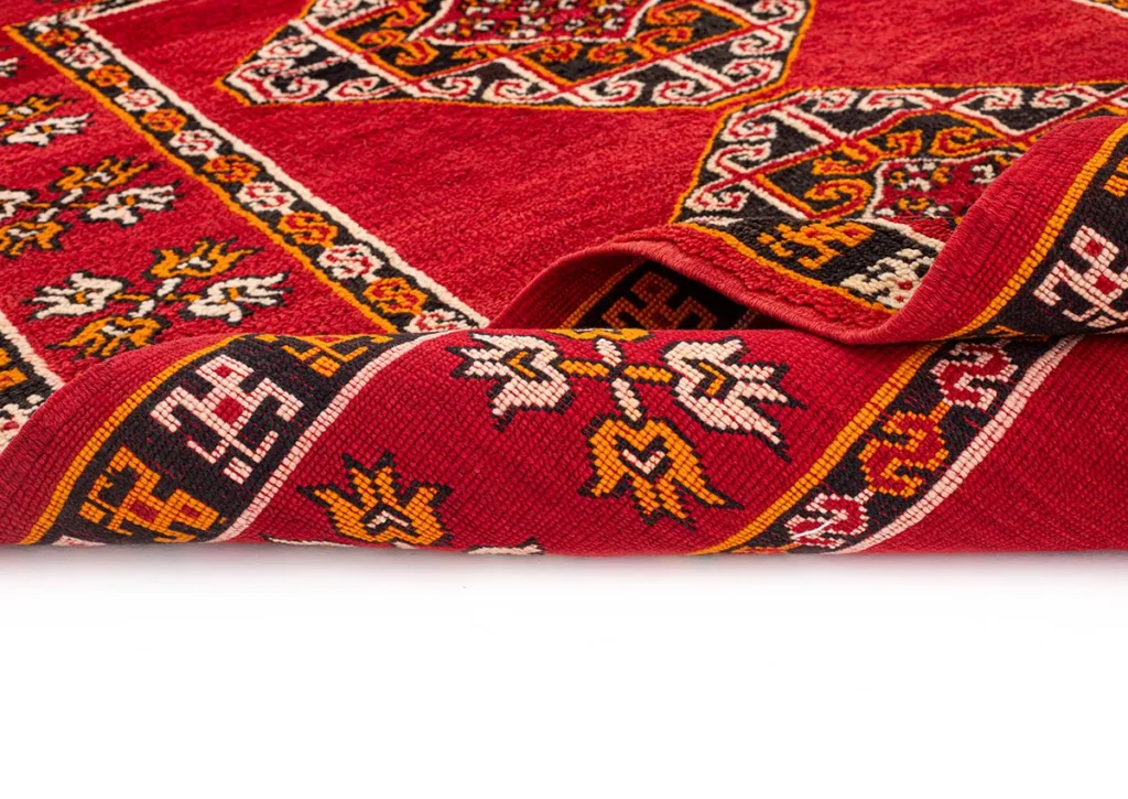 A beautifully crafted red and multicolored woven rug featuring intricate geometric and floral designs, with one edge elegantly rolled.