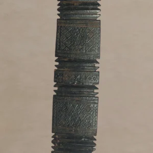 Hand-carved vintage wooden object with intricate geometric patterns and ridges, reminiscent of an ornately designed tent peg, shown against a neutral background.