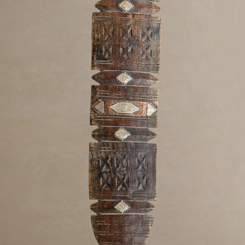 An intricately carved wooden pillar, reminiscent of vintage wooden tent pegs, features geometric and diamond-shaped patterns, displayed on a light brown background.