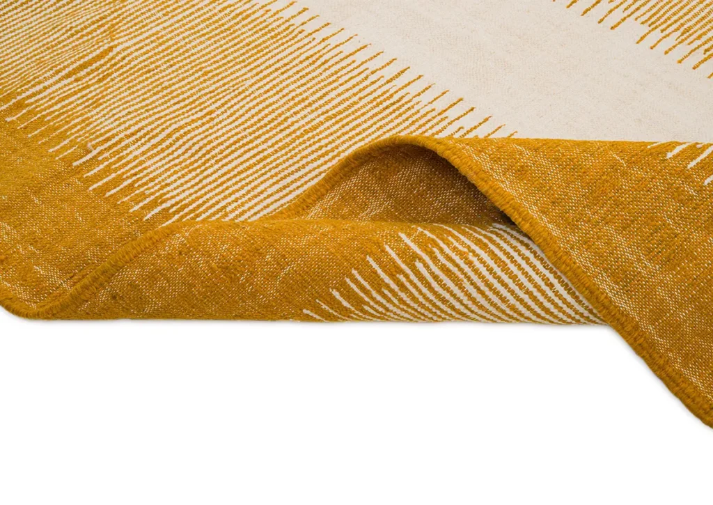 A close-up of a woven rugs corner reveals a beautiful yellow and white pattern, with the edge playfully turned up.