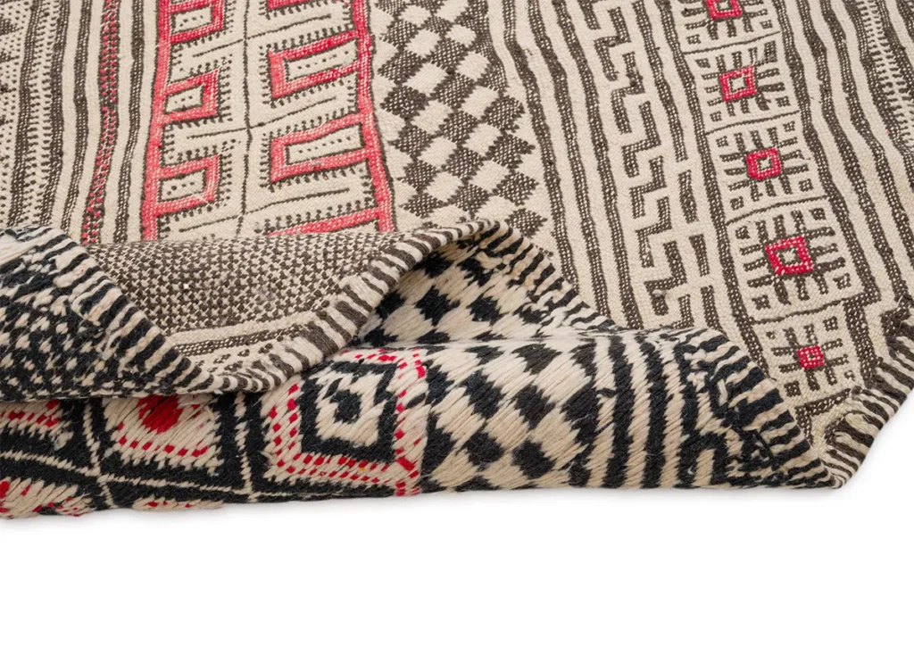 A vintage handwoven rug featuring a folded geometric pattern with striking red, black, and beige designs.