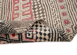 A vintage handwoven rug featuring a folded geometric pattern with striking red, black, and beige designs.