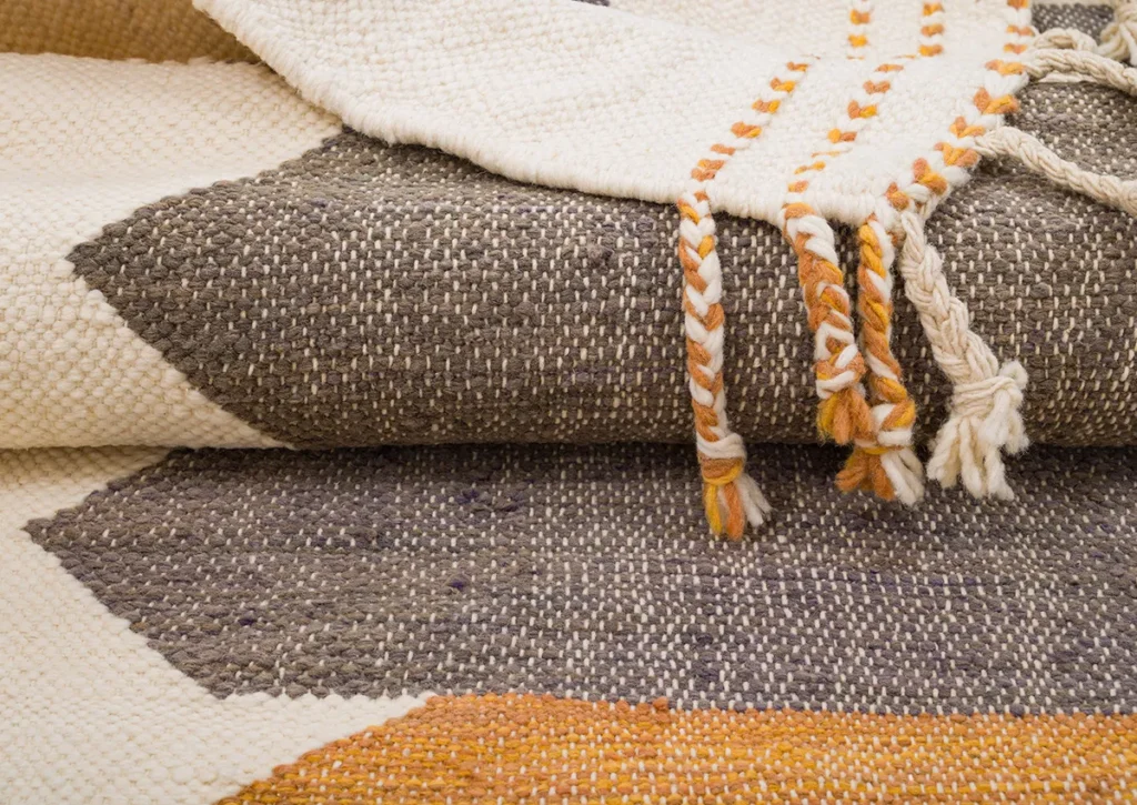 Woven textiles showcase geometric patterns in brown, cream, and orange tones, accented with braided tassels on the edge.