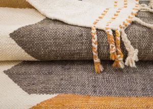 Woven textiles showcase geometric patterns in brown, cream, and orange tones, accented with braided tassels on the edge.