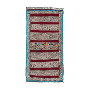 A vibrant woven rug with geometric patterns, showcasing bold red, white, and multicolored sections, framed by a striking blue border.