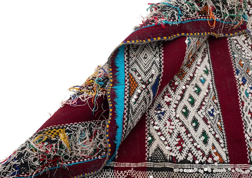 A close-up of a vibrant, intricately woven textile showcases geometric patterns and fringed edges, with an array of colors including red, white, and blue.