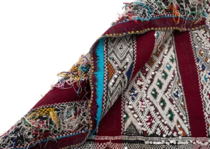 A close-up of a vibrant, intricately woven textile showcases geometric patterns and fringed edges, with an array of colors including red, white, and blue.