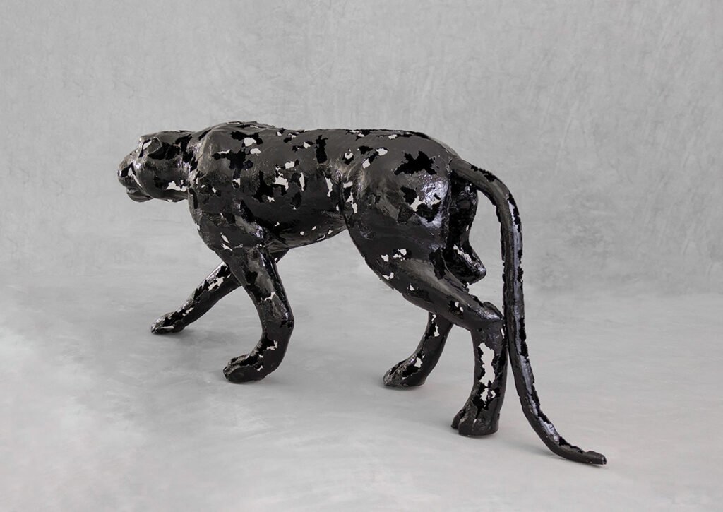A striking panther metalwork sculpture with a glossy speckled texture stands on all fours against a plain gray background.