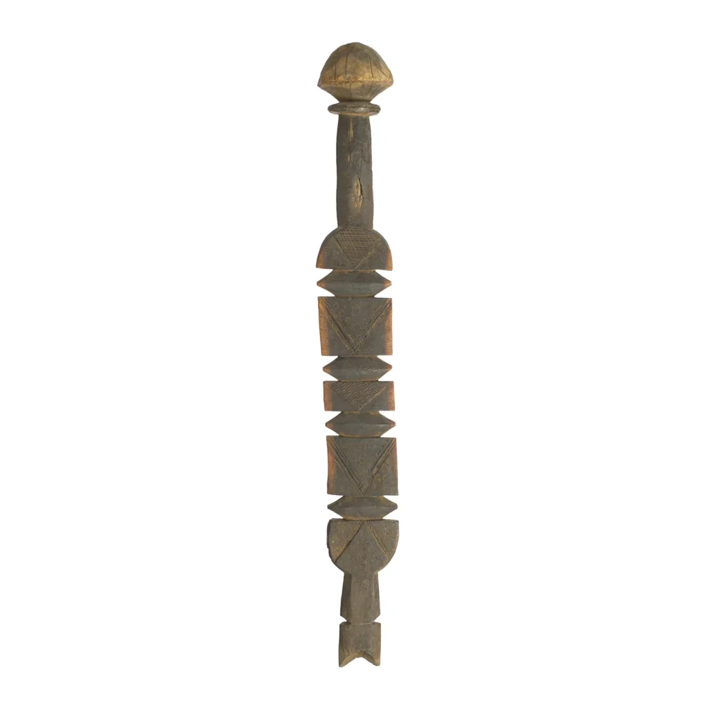 A carved wooden sculpture with abstract geometric shapes, reminiscent of vintage wooden tent pegs, stands upright.