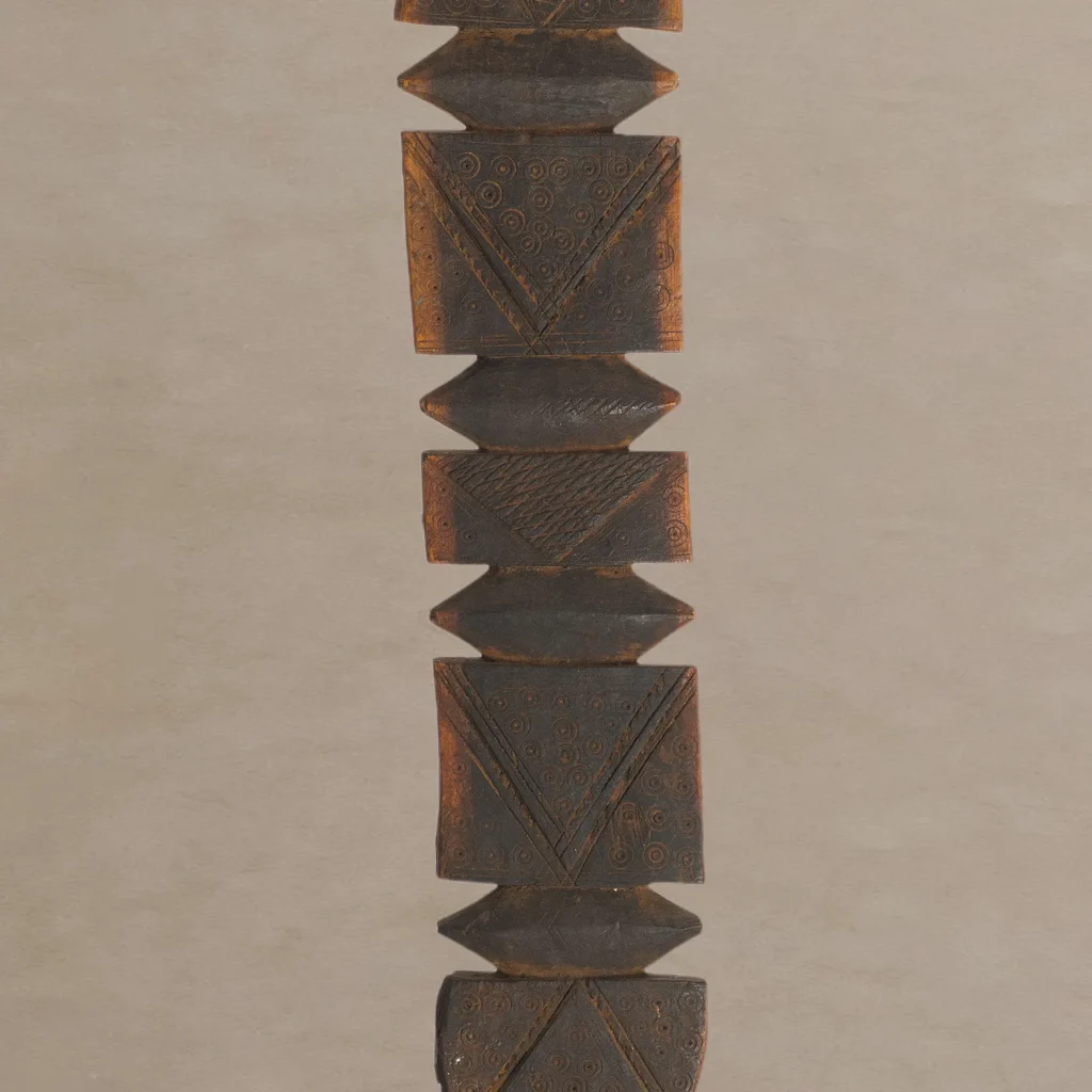 A vintage wooden carving, reminiscent of rustic tent pegs, showcases intricate geometric patterns and designs in rich brown and black tones, elegantly displayed against a plain backdrop.