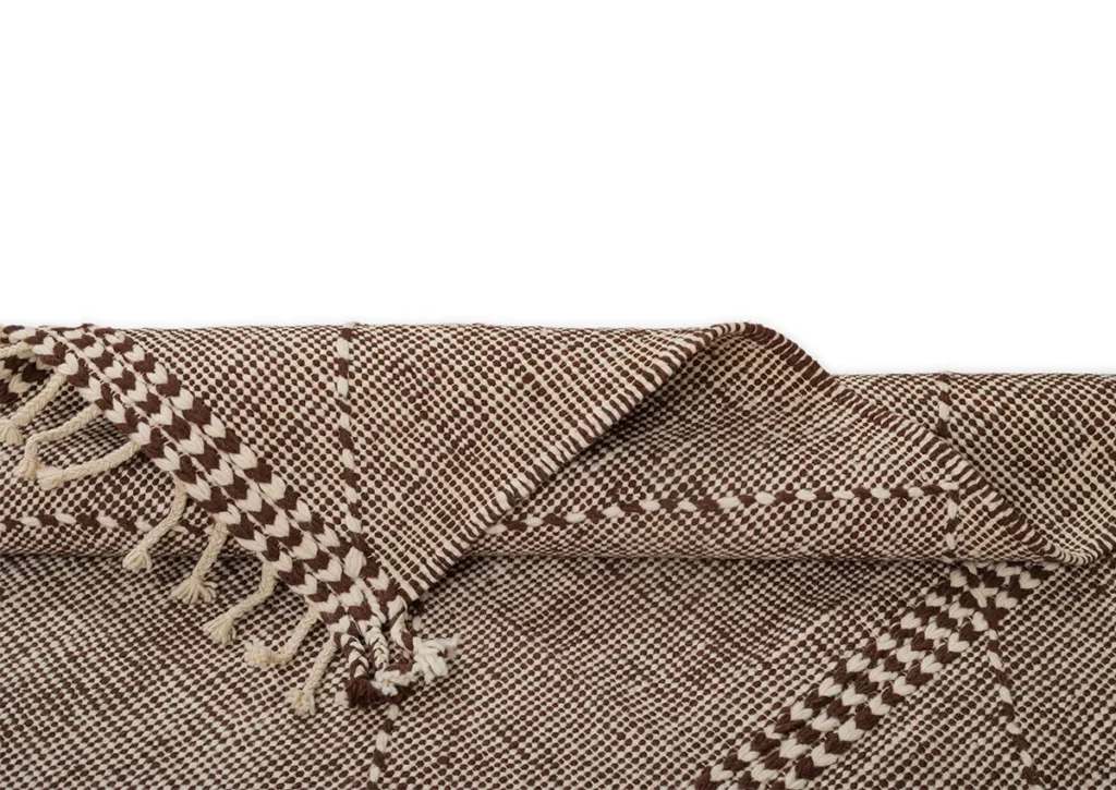 A woven brown and white textile with fringed edges, artfully folded at one corner against a crisp white background.