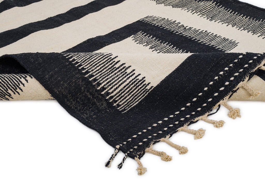 A close-up of a folded black and white woven textile with a geometric pattern and a tasseled edge, exuding modern elegance.