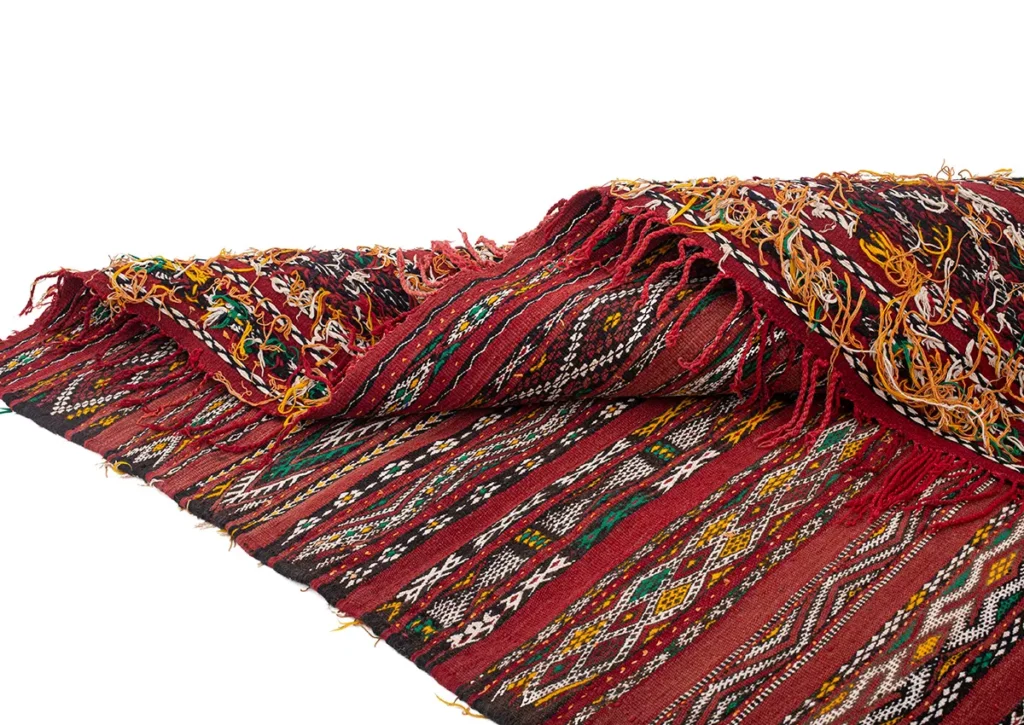 A vintage handwoven rug with intricate geometric patterns in red, yellow, green, black, and white, featuring fringed edges.