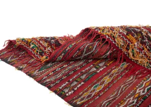 A vintage handwoven rug with intricate geometric patterns in red, yellow, green, black, and white, featuring fringed edges.