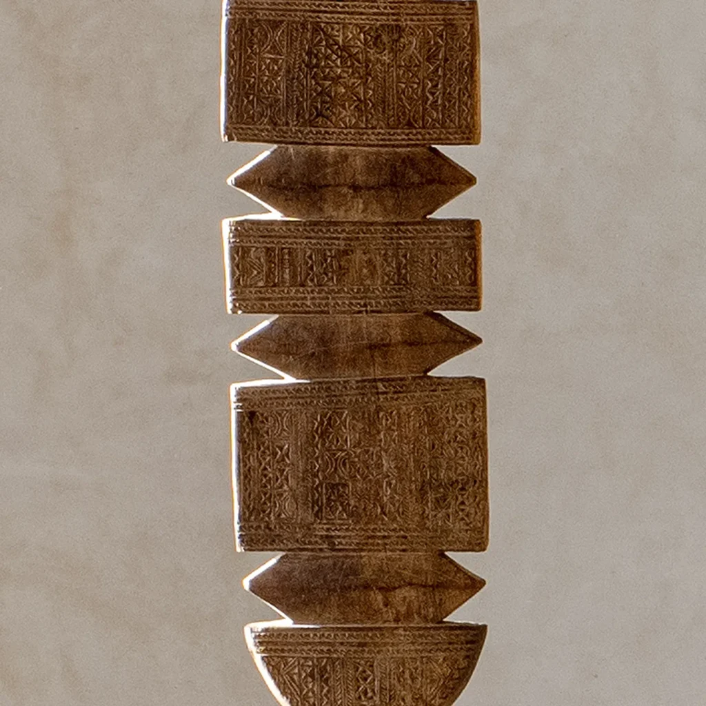 Hand-carved stone pillar adorned with geometric and floral patterns, reminiscent of a vintage wooden tent peg, elegantly set against a plain backdrop.