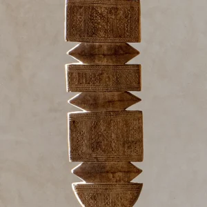 Hand-carved stone pillar adorned with geometric and floral patterns, reminiscent of a vintage wooden tent peg, elegantly set against a plain backdrop.