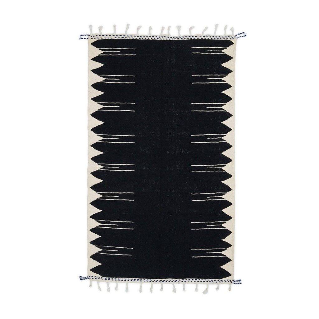 Handwoven black and white geometric patterned rug with fringe on the short edges.