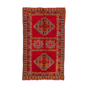 A rectangular red rug featuring intricate geometric patterns is accented with black, green, and yellow on a white background. This elegant design adds a vibrant touch to any living space.