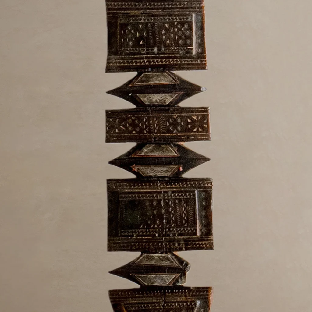 Close-up of an ornate, hand-carved geometric artifact against a neutral background, reminiscent of a vintage wooden tent peg with intricate carvings and symmetrical patterns.