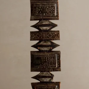 Close-up of an ornate, hand-carved geometric artifact against a neutral background, reminiscent of a vintage wooden tent peg with intricate carvings and symmetrical patterns.