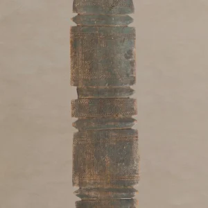 A tall, hand-carved wooden artifact with vintage geometric patterns, reminiscent of an elegant tent peg, stands vertically against a plain background.