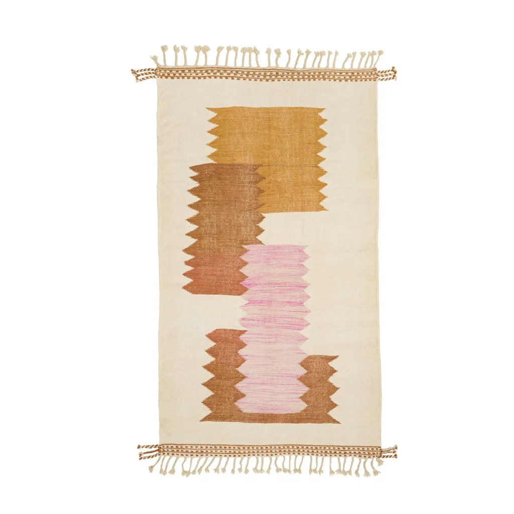 This rectangular woven rug, complete with tasseled edges, boasts an intricate design of three zigzag vertical patterns in brown, pink, and gold set against a cream background. Its artistic flair adds a vibrant touch to any space.