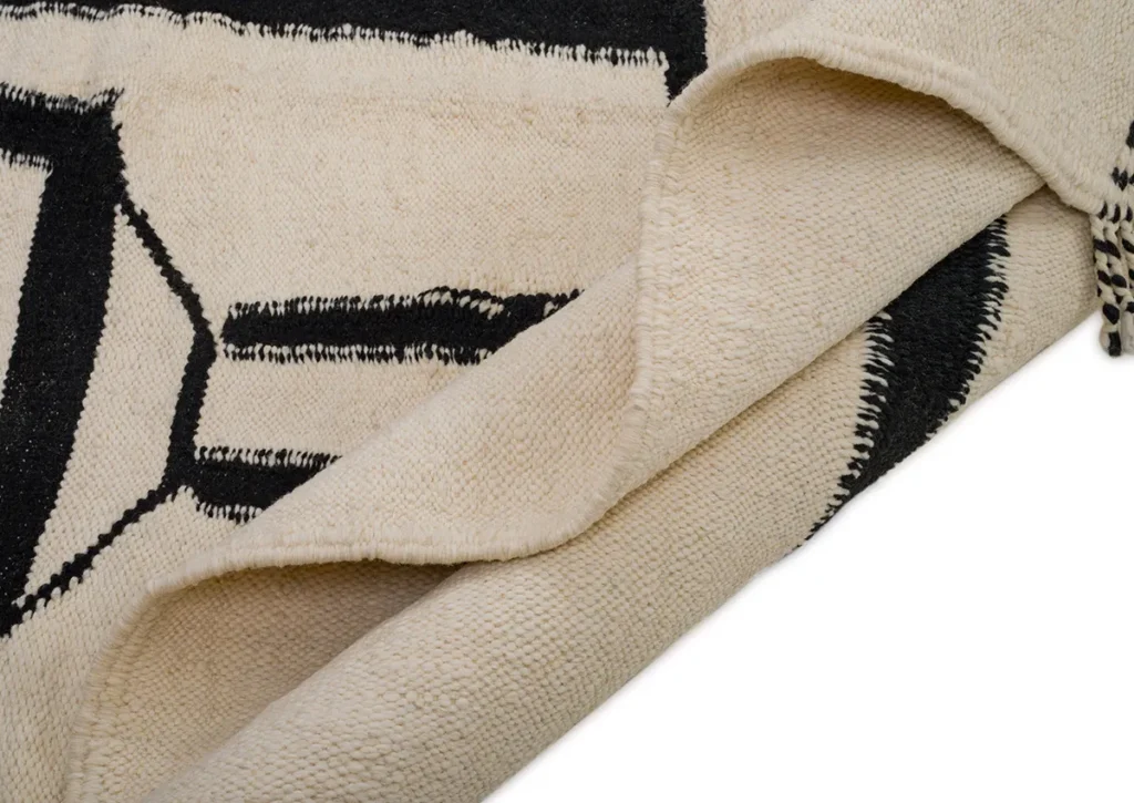 A close-up of a textured beige rug with black geometric patterns, featuring beautifully folded edges, adds a touch of sophistication and style to any room.