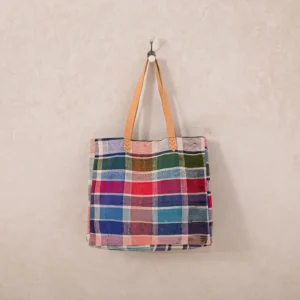 A colorful plaid tote bag with tan leather handles hangs on a wall hook.