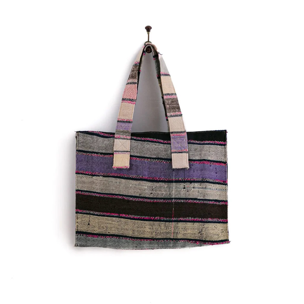 A multicolored striped tote bag with two handles hangs on a wall hook.