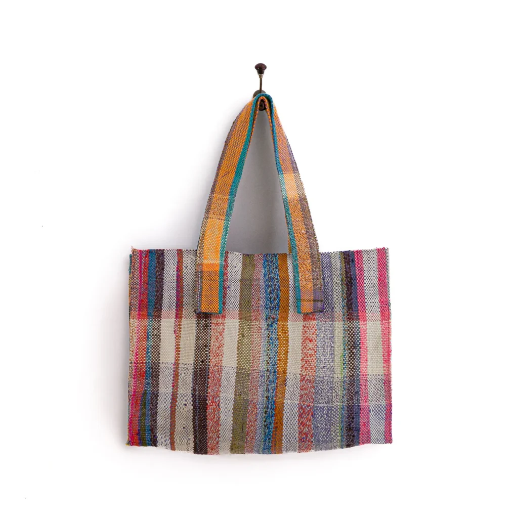 A multicolored striped woven tote bag hangs on a wall hook.