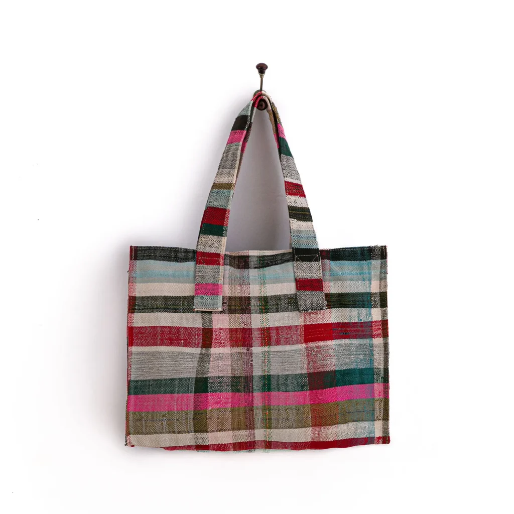 Multicolored, striped tote bag hanging on a wall hook, featuring pink, red, green, and blue hues.