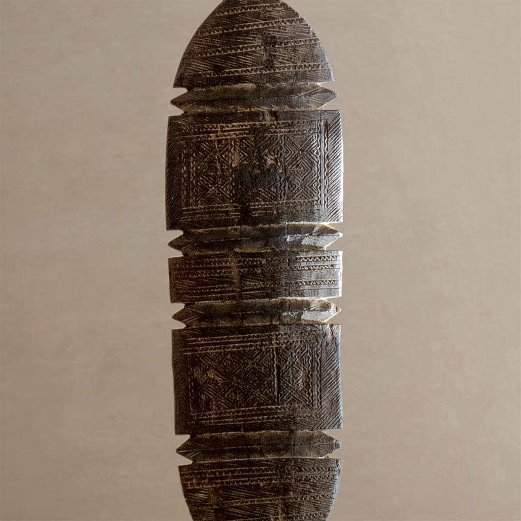 A vintage wooden object with intricate geometric patterns, reminiscent of ornate tent pegs, features symmetrical segments and a pointed top and bottom, set against a plain background.