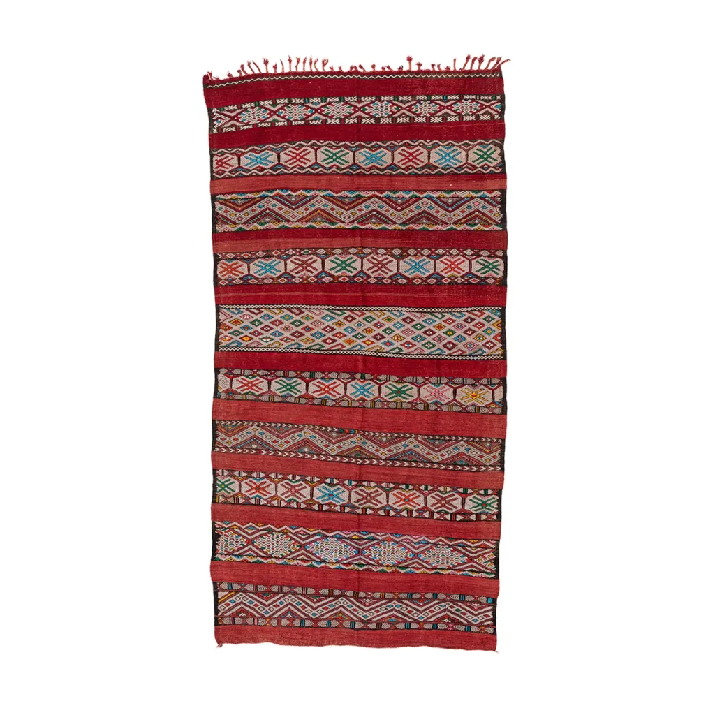 A traditional woven rug adorned with red, green, and white geometric patterns and fringed edges adds a touch of cultural elegance to any space.