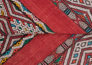 Close-up of a vintage handwoven rug with intricate geometric patterns in red, white, yellow, blue, and green, showcasing diagonal stripes and diamond shapes.