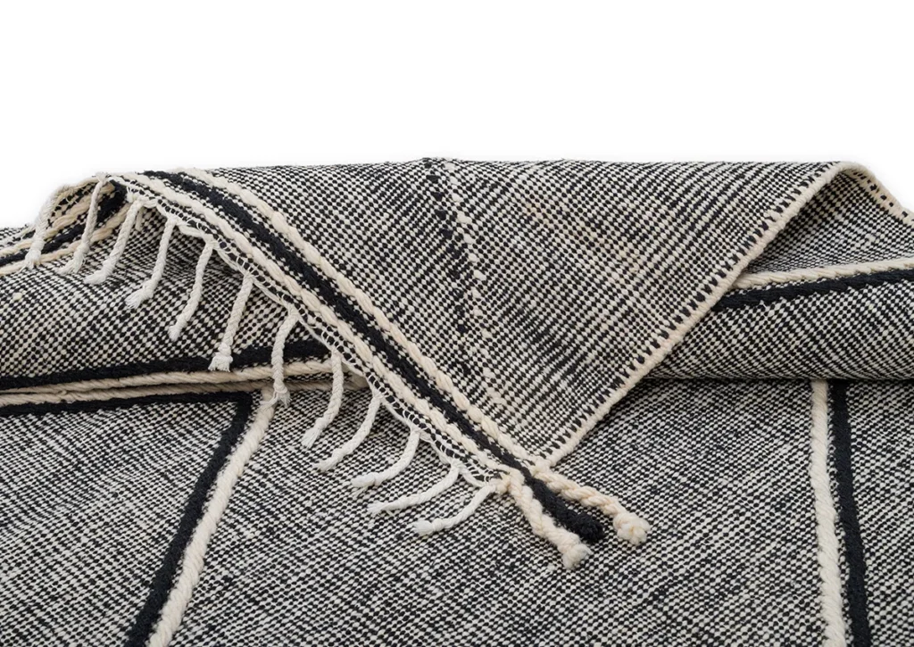 A folded black and white woven creation features intricate fringe detailing on the edges, adding an elegant touch.