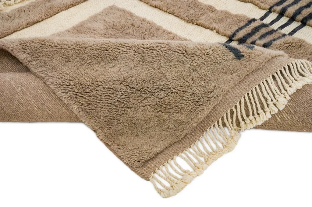 This luxury Moroccan rug showcases intricate geometric patterns and elegant striped elements in beige and brown tones, complete with delicate fringe detailing.