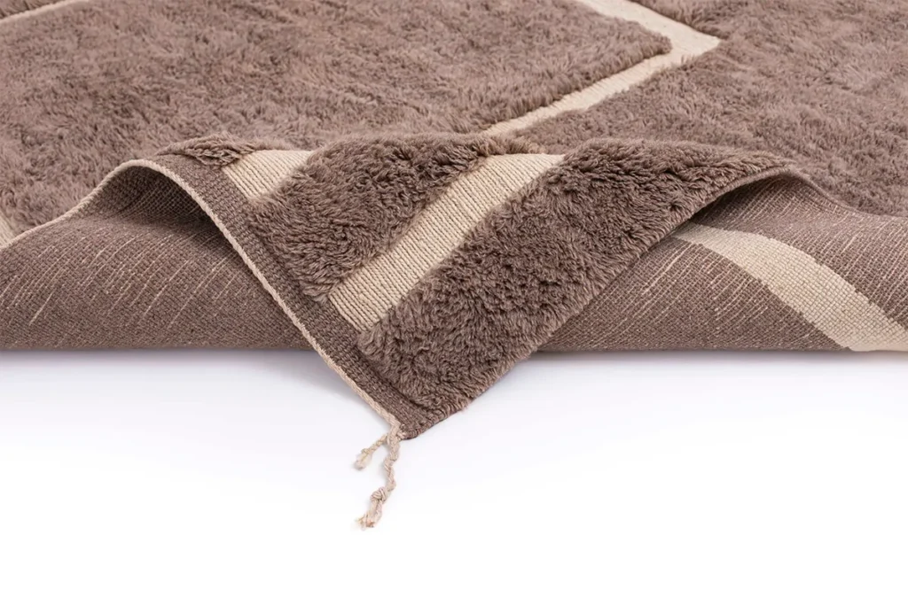 A luxurious hand-knotted brown rug with a textured surface and beige striped edges is elegantly displayed on a white surface.